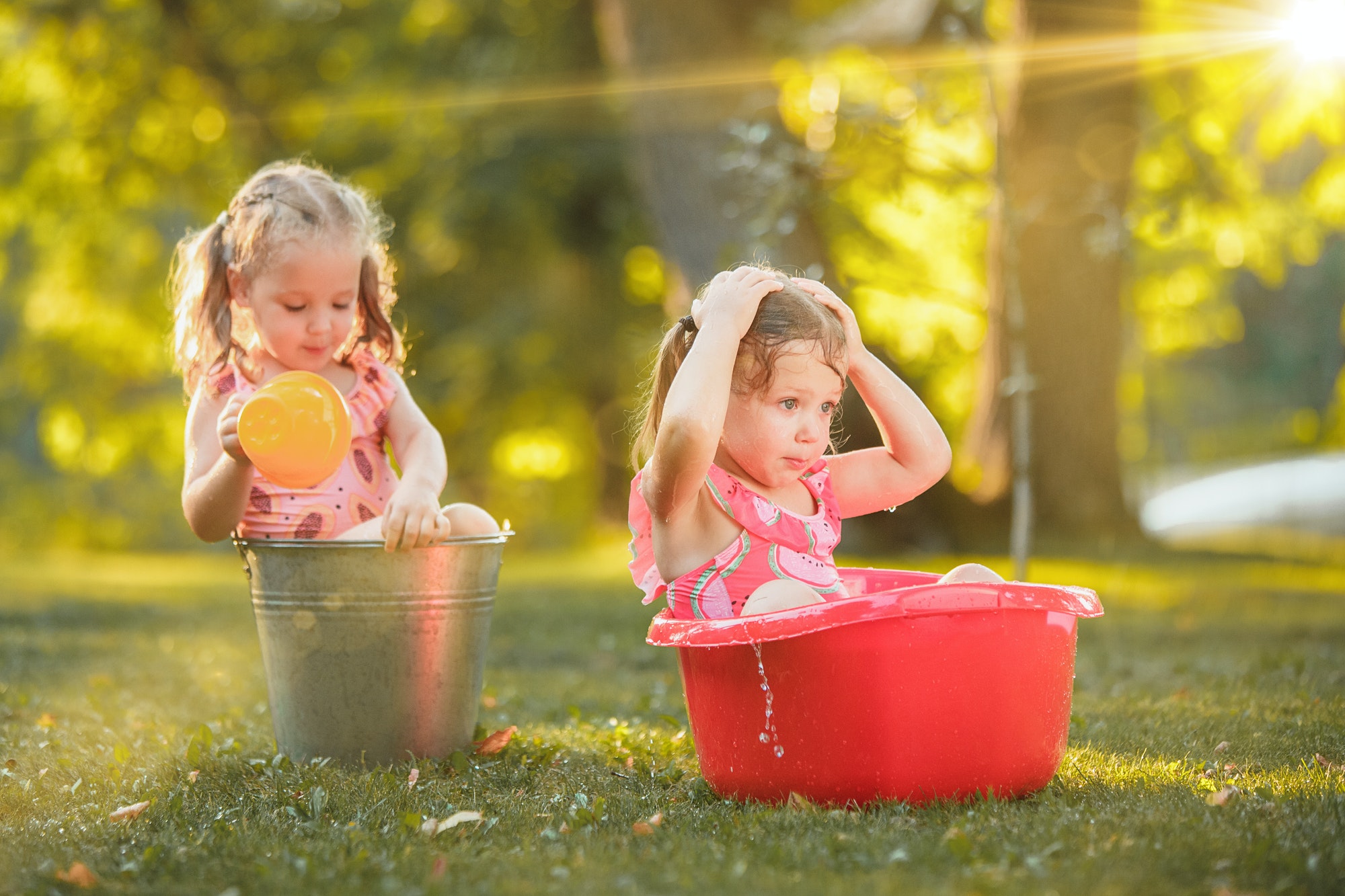 The cute little blond girls playing with water splashes on the field in summer